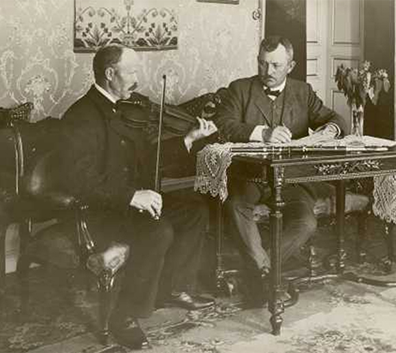 Svartvitt foto av tv&aring; personer. En spelar fiol och en skriver.